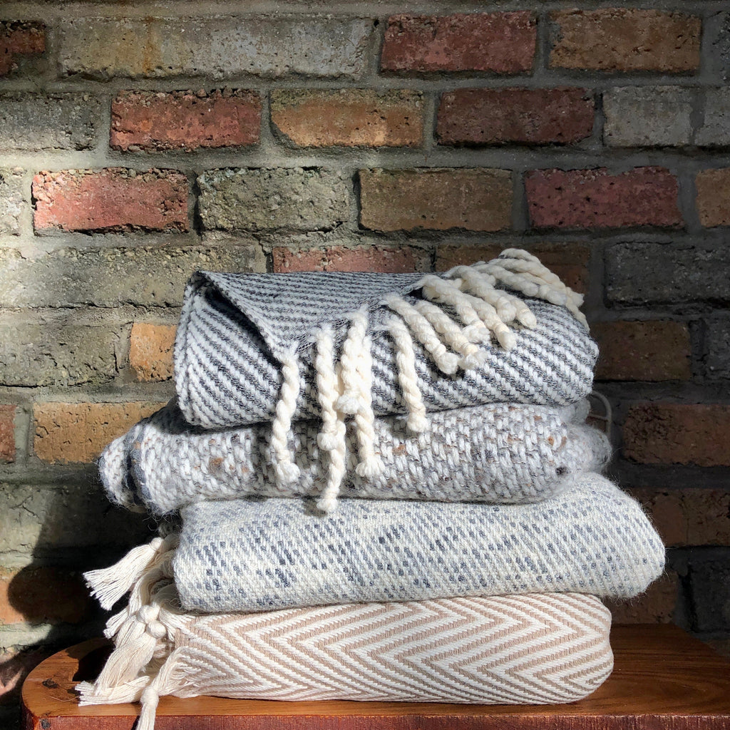 Stack of textured blankets with tassels against a brick wall